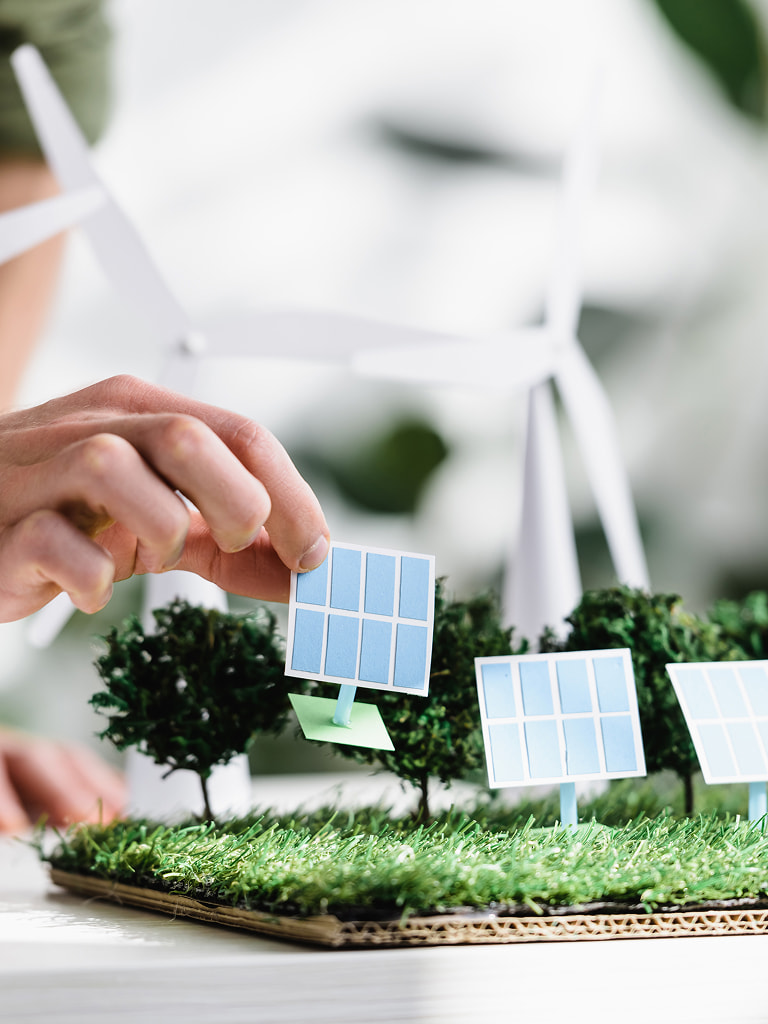 Ręka ustawiająca model panelu słonecznego w makiecie z turbinami wiatrowymi